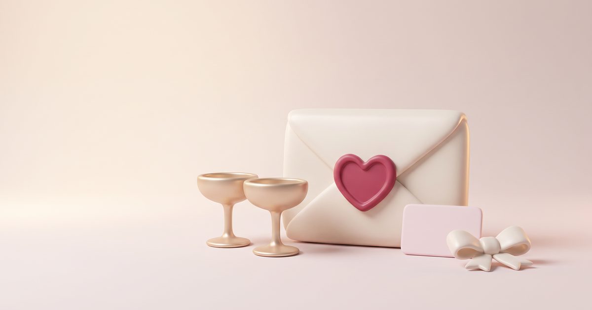 A cream envelope with a rose wax heart, two small gold coupe glasses and a blush card standing beside it