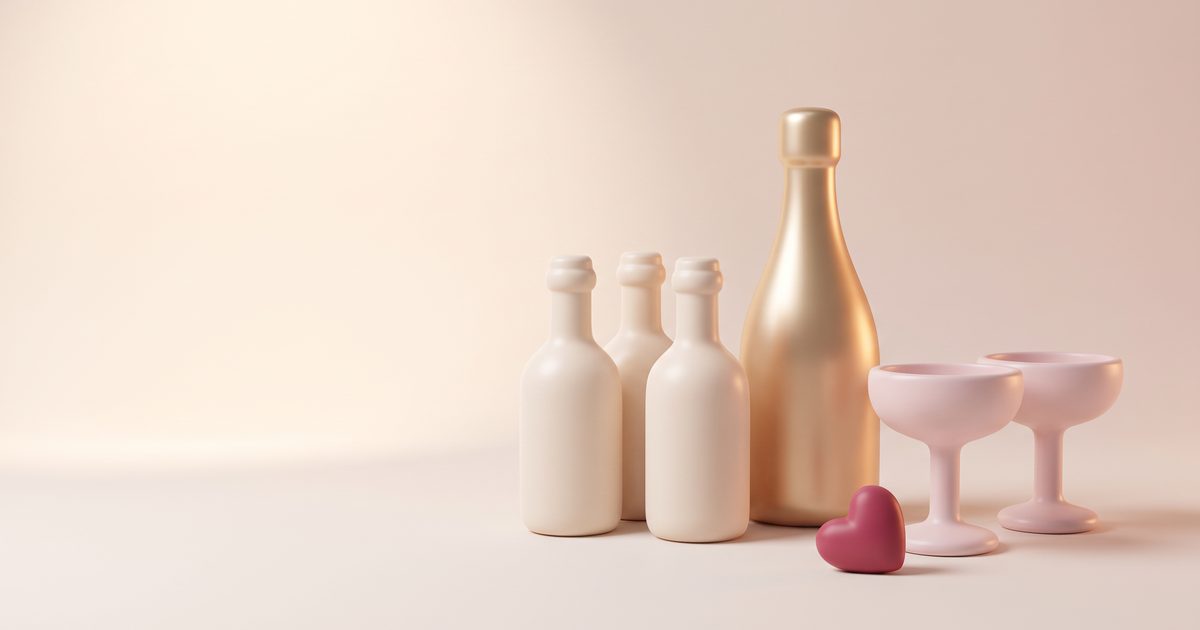 Small cream wine bottles and a gold bottle beside two blush glasses and a rose heart