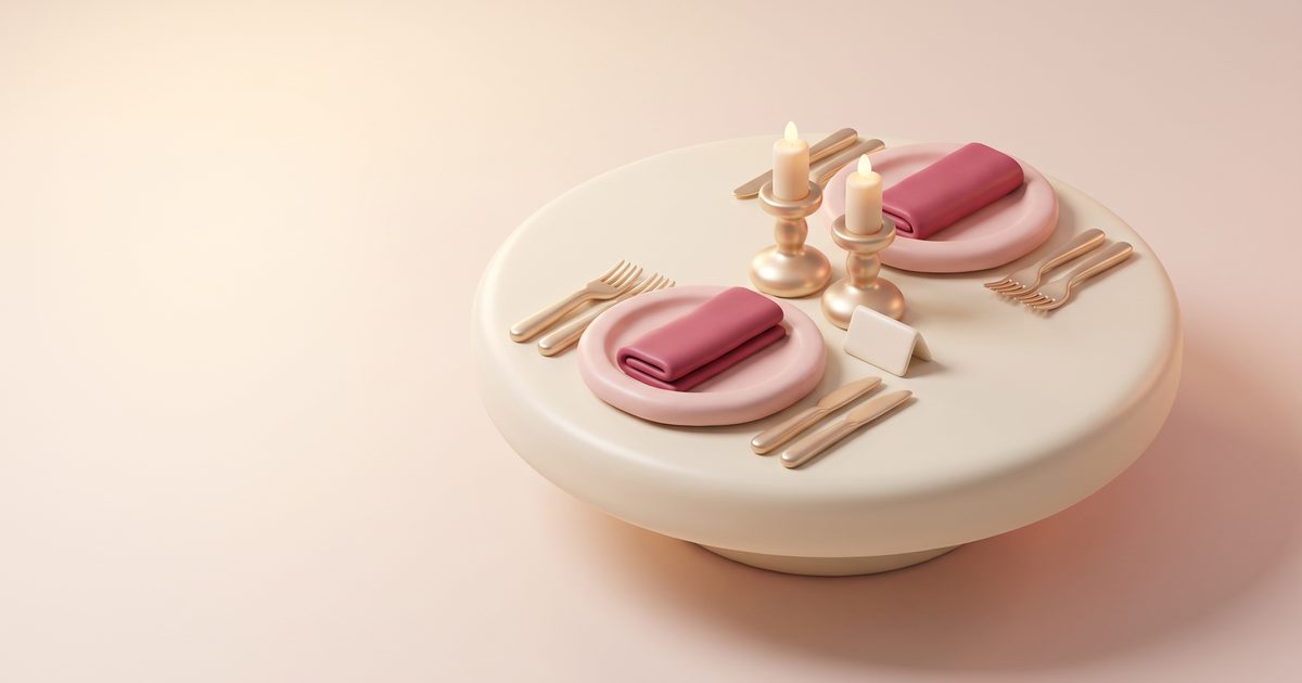 A small round table set with blush plates, gold cutlery and two gold candlesticks