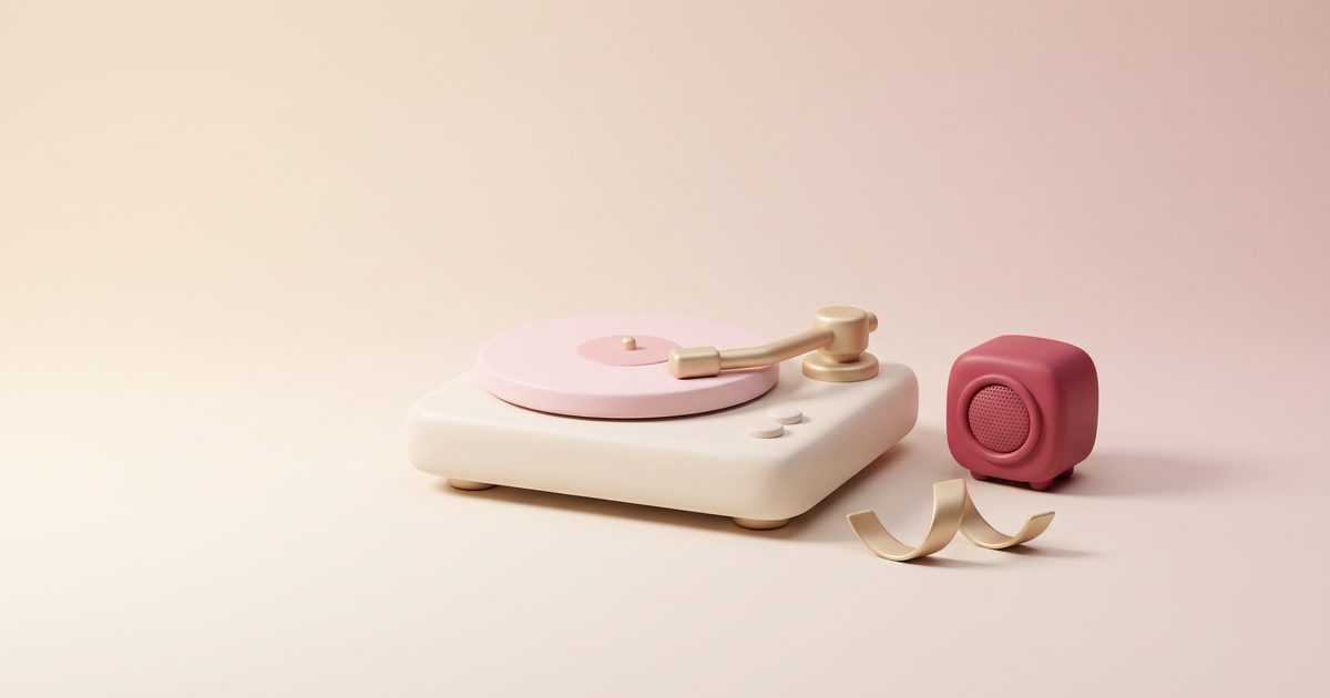A cream record player with a gold arm and a blush record beside a small rose speaker and a gold ribbon