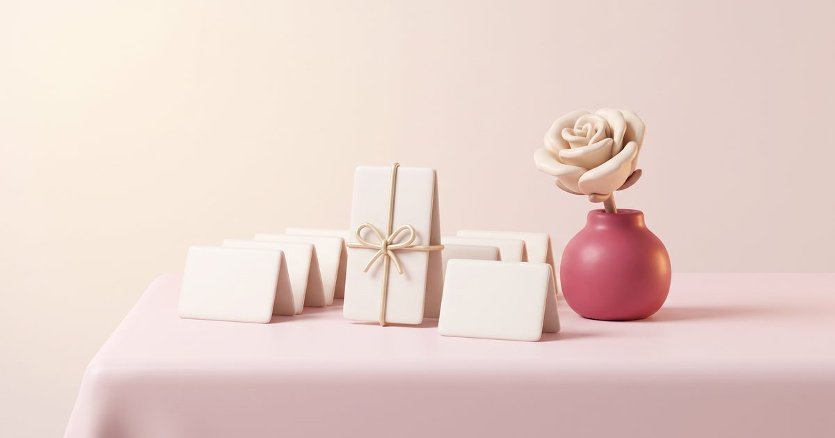 A row of small folded cream cards on a blush tablecloth beside a rose bud vase