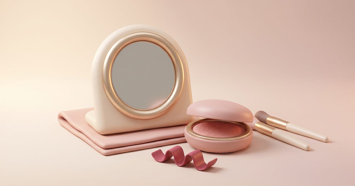 A cream vanity mirror with a gold rim beside a blush compact, two makeup brushes and a rose ribbon