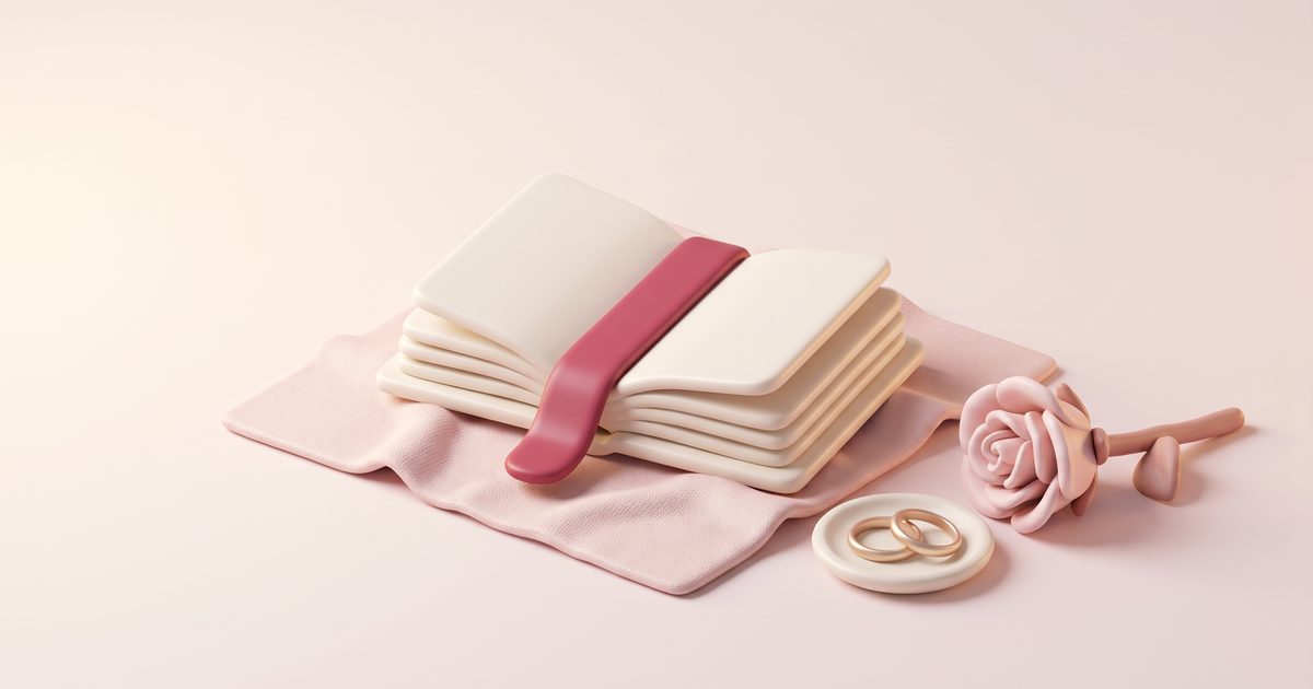 An open cream book with a rose ribbon bookmark beside two gold rings on a small dish and a blush rose
