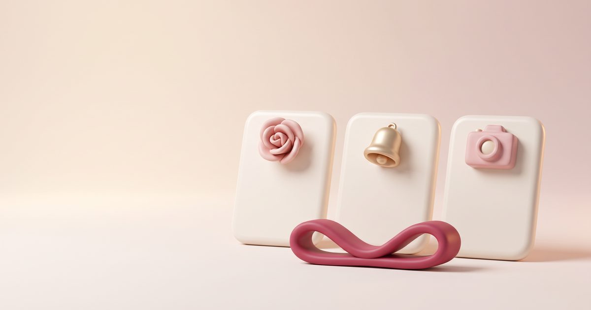 Three cream cards standing in a row, topped with a clay rose, a gold bell and a blush camera, with a rose ribbon in front