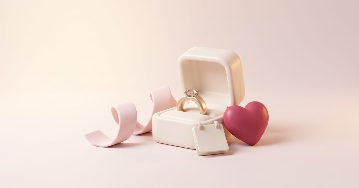 An open cream ring box with a gold ring beside a blush ribbon, a blank calendar page and a small rose heart
